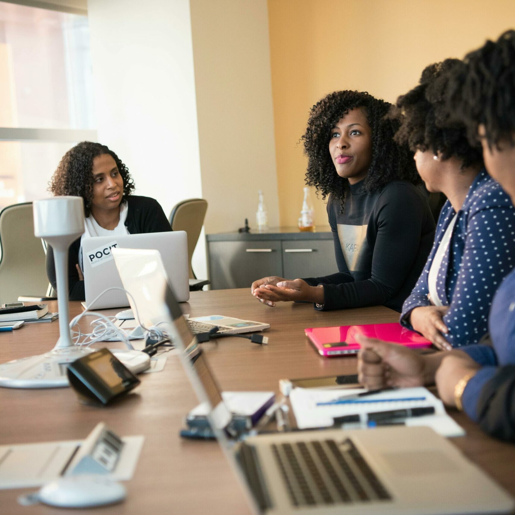 Five women sitting at a conference table discussing