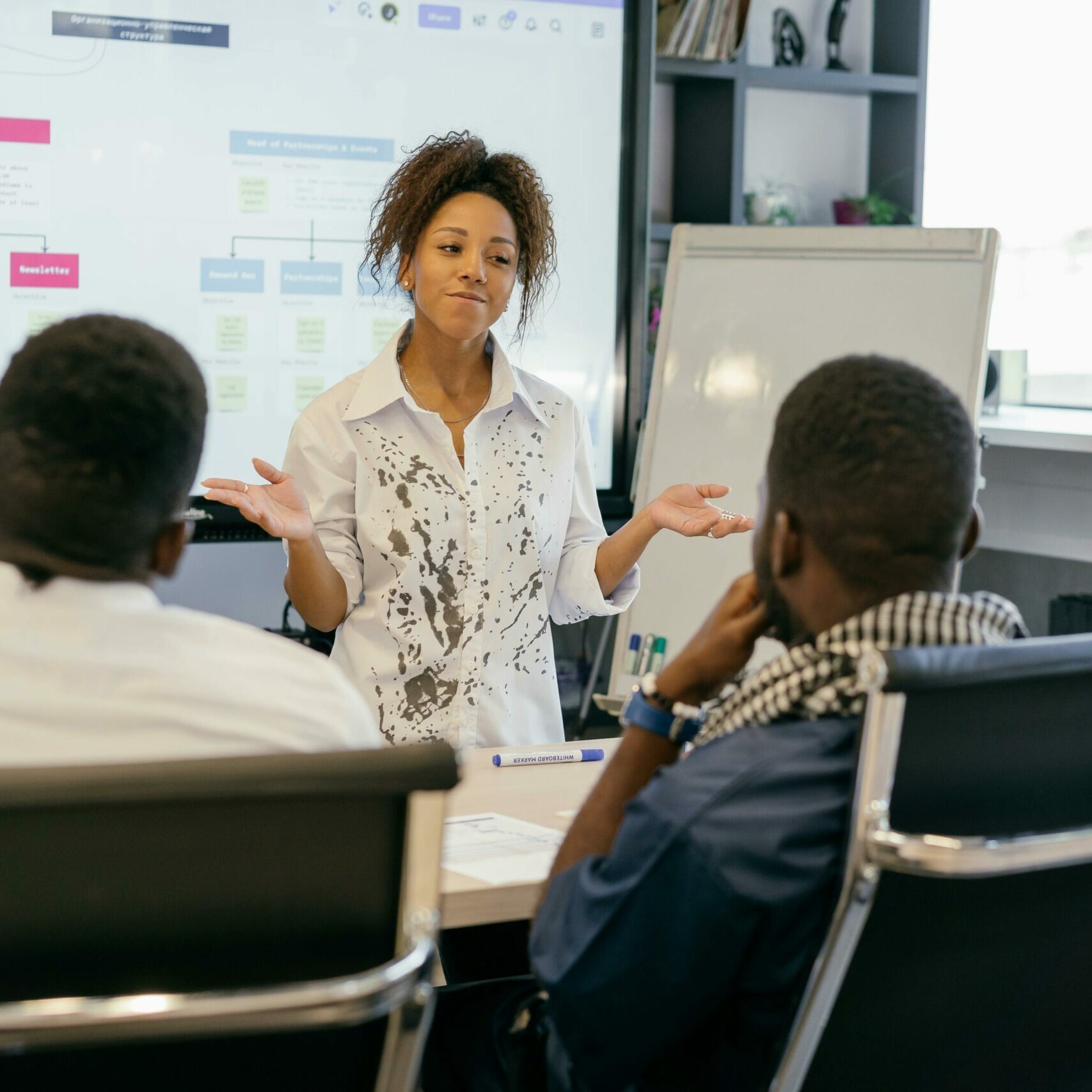 A woman in a meeting room making a visual presentation to her two peers.