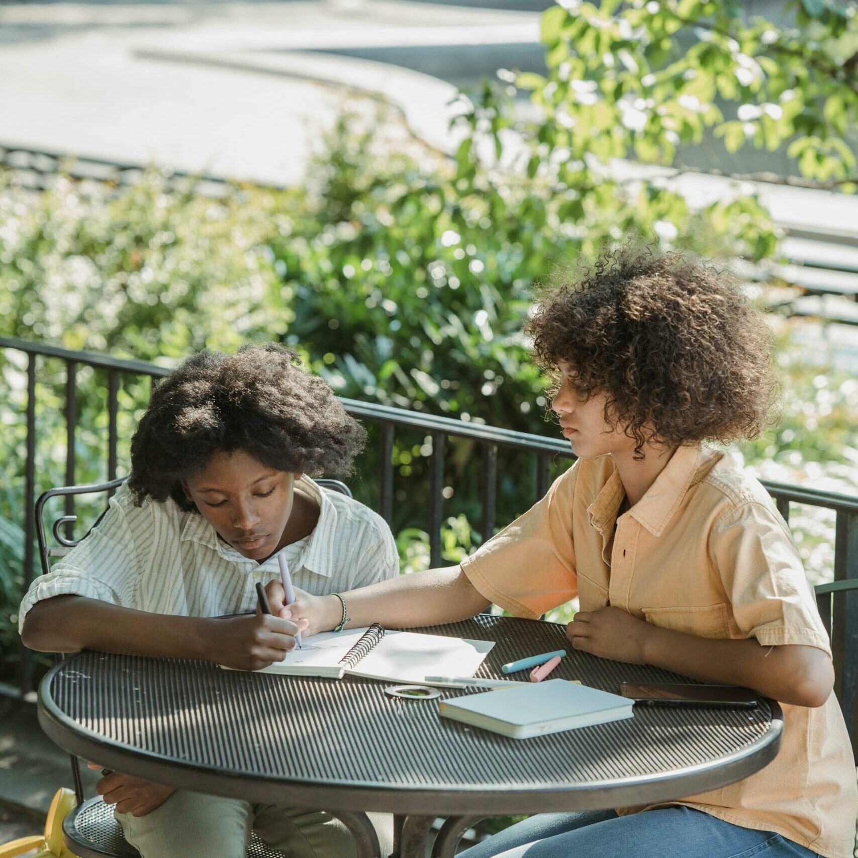 Two women sitting at a table outside helping each other with homework